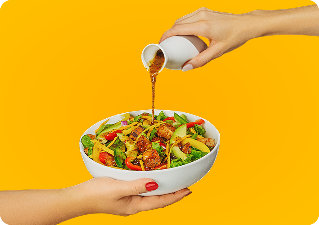 Chef pouring dressing over a fresh salad bowl